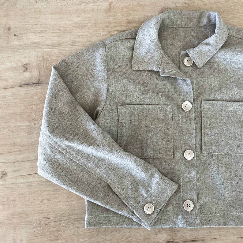 May include: A gray cropped jacket with long sleeves and four buttons down the front. The jacket has two large pockets on the front.