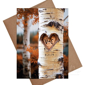 May include: A greeting card featuring a photograph of a birch tree trunk with a heart carved into it. The heart contains the initials "V+G" and the date "8.23.19". The card is set against a backdrop of fall foliage and a brown envelope.