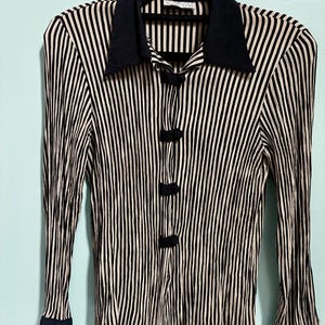 May include: A long-sleeved shirt with vertical black and beige stripes. The shirt has a dark navy collar, cuffs, and three button closures. The brand name "NOTIONS" is visible on the collar.