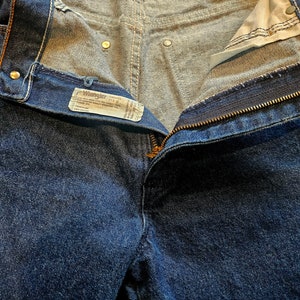 May include: A pair of blue denim jeans with a zipper fly and a Wrangler label. The jeans are unbuttoned and the waistband is folded down.