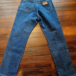 May include: A pair of blue denim jeans with a brown leather Wrangler label on the back pocket.