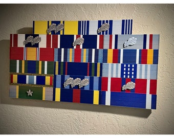 May include: A display of military ribbons and medals, including a variety of colors and designs. The ribbons are arranged in rows and columns, and there are several medals attached to the ribbons. The medals are silver and have a leaf design.