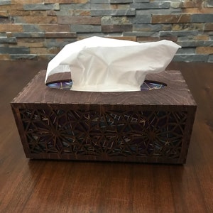 May include: A wooden tissue box cover with a geometric design. The cover is dark brown with a black and purple geometric pattern. The tissue box is made of wood and has a clear plastic window.