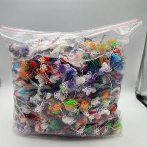May include: A clear plastic bag filled with a large assortment of colorful yarn scraps. The yarn pieces are various colors, including red, orange, blue, green, purple, and white. The bag is sealed with a red zipper.