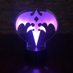 May include: A purple and white LED night light shaped like a bat with a diamond in the center. The light is on and illuminating the room.
