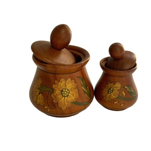 Puede incluir: Dos botes de madera con tapas, pintados con flores amarillas y hojas verdes. Los botes son marrones y tienen un aspecto rústico.