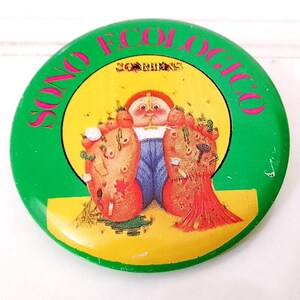 Puede incluir: Un botón redondo verde y amarillo con el texto "SONO ECOLOGICO" en letras rosas. El botón presenta una ilustración de dibujos animados de un niño de pelo rojo con una camisa azul y pantalones verdes sentado en una cama de hojas verdes. El texto "SORRISO" es visible en la parte superior del botón.