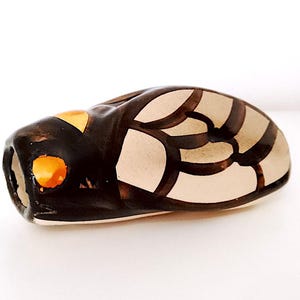 May include: A ceramic figurine of a cicada with brown, white and orange details. The cicada is painted with a geometric pattern.