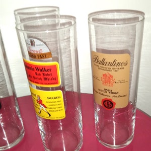 May include: Four clear glass tumblers with labels for Johnnie Walker Red Label Scotch Whisky and Ballantines Finest Scotch Whisky. The labels are in yellow, red, and brown.