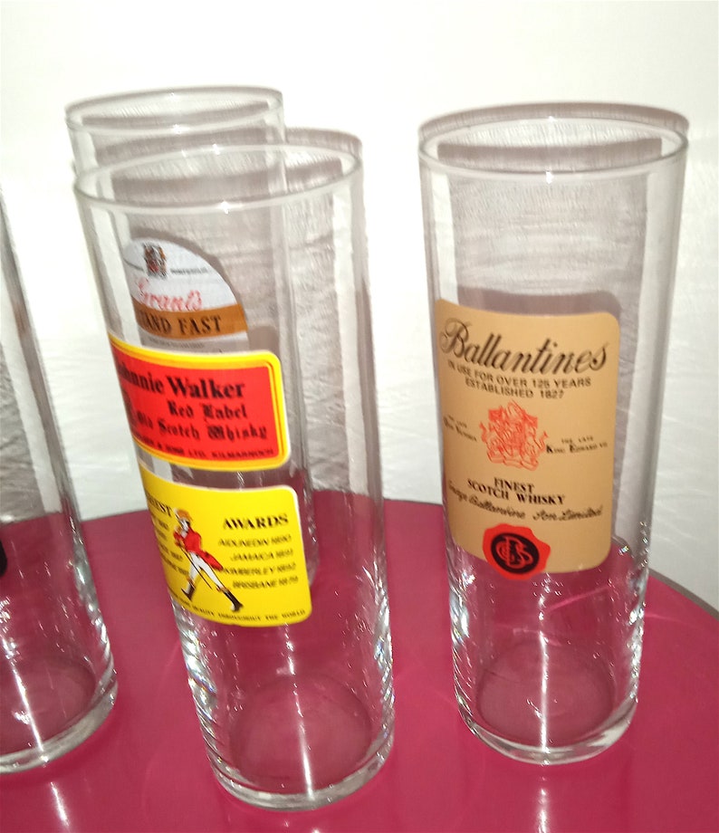 May include: Four clear glass tumblers with labels for Johnnie Walker Red Label Scotch Whisky and Ballantines Finest Scotch Whisky. The labels are in yellow, red, and brown.