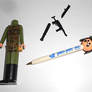 May include: A green camouflage military figure with a black belt and a brown pouch. The figure is missing its head. There is a black pen with a blue and white label that says "pen-pen" and a soldier head eraser on the end. There is also a black knife, a black baton, and a black rifle.