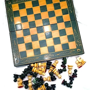 Peut inclure: Un jeu d'échecs en bois avec un plateau vert et marron et des pièces noires et blanches. Le plateau est fermé et les pièces sont éparpillées sur une surface blanche. Le plateau porte l'inscription "Matteo".