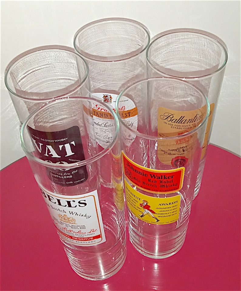 May include: Five clear glass tumblers with different Scotch whisky labels. The labels include "VAT 69", "Bell's", "Grants", "Ballantine's", and "Johnnie Walker Red Label".