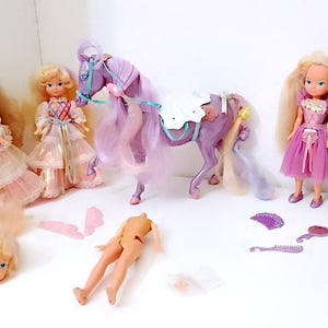 Peut inclure: Un ensemble de cinq poupées vintage, dont quatre princesses et un cheval violet. Les princesses portent des robes roses, blanches et bleues avec des détails en dentelle. Le cheval a une selle blanche et une crinière et une queue longues et flottantes.