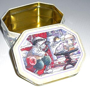 Può includere: Una scatola di latta vintage con un'illustrazione colorata di un tasso e un riccio. Il tasso indossa un gilet e tiene una pipa. Il riccio è a letto con una coperta e una lampada sul comodino. La scatola di latta è perfetta per riporre piccoli oggetti.