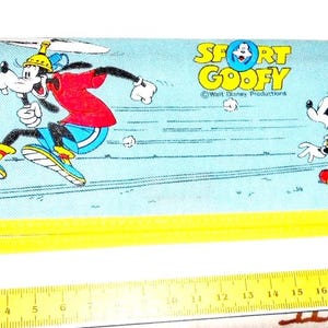 Peut inclure: Une trousse à crayons bleue et jaune avec une image de dessin animé de Goofy courant et Mickey Mouse regardant. Le texte "Sport Goofy" et "Walt Disney Productions" est imprimé sur la trousse.