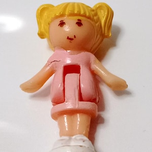 Può includere: Statuina di bambola vintage con codini biondi, indossa un vestito rosa e scarpe bianche. La bambola ha un piccolo viso con lineamenti dipinti e braccia tese. Un giocattolo da collezione.