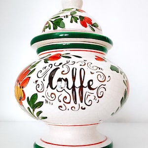 Può includere: Barattolo per caffè in ceramica bianca con coperchio verde e decorazioni floreali. Il barattolo ha la scritta "Caffe" in corsivo marrone.