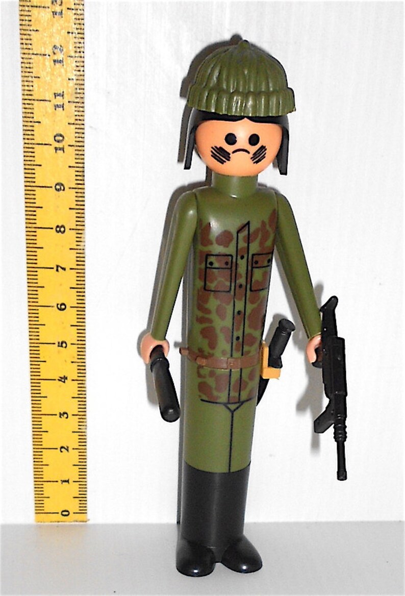 May include: A green plastic toy soldier figure wearing a green camouflage uniform, a black hat, and holding a black rifle and a black baton.