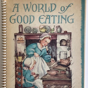 Peut inclure: Un livre de cuisine vintage intitulé "A World of Good Eating: Recipes from Around the World". La couverture présente une illustration de deux filles dans une cuisine, l'une remuant une casserole et l'autre assise à une table.