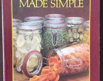 May include: A maroon hardcover book titled Dehydration Made Simple by Mary Bell. The cover features a collection of clear glass jars with metal wire-bail closures, filled with various dried foods like orange apricots, green peas, and sliced apples.