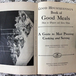 May include: A vintage cookbook titled "Good Housekeeping's Book of Good Meals: How to Prepare and Serve Them" with a guide to meal planning, cooking, and serving. The cover features a black and white photo of a table setting with candles and silverware.