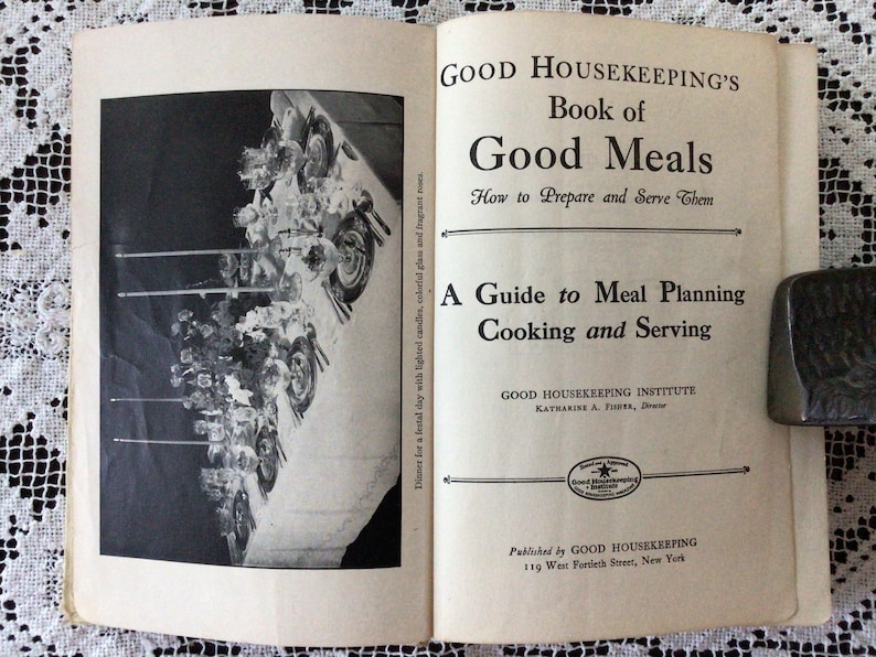 May include: A vintage cookbook titled "Good Housekeeping's Book of Good Meals: How to Prepare and Serve Them" with a guide to meal planning, cooking, and serving. The cover features a black and white photo of a table setting with candles and silverware.