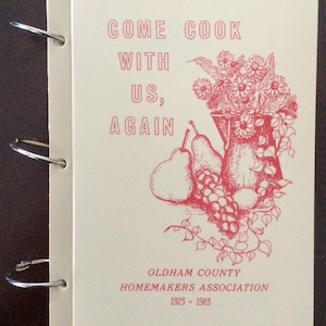 Peut inclure: Un livre de cuisine crème avec du texte et des illustrations rouges. La couverture indique "COME COOK WITH US, AGAIN" au-dessus d'un dessin d'un vase de fleurs, de poires et de raisins. Le bas indique "OLDHAM COUNTY HOMEMAKERS ASSOCIATION 1923-1983".