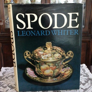 May include: A book titled "Spode" by Leonard Whiter, featuring a colorful porcelain tureen with a lid and a matching saucer. The tureen is decorated with floral and fruit motifs, and the saucer has a pink rose design.