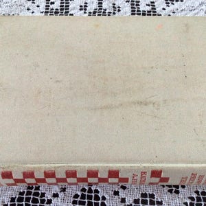 May include: A vintage cookbook with a white cover and a red and white checkered spine. The title on the spine reads "Good Meals and How to Make Them".