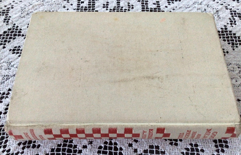 May include: A vintage cookbook with a white cover and a red and white checkered spine. The title on the spine reads "Good Meals and How to Make Them".