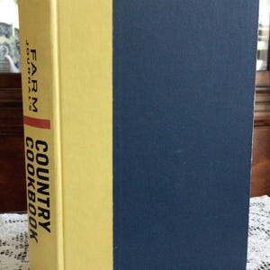 May include: A vintage hardcover cookbook with a yellow spine and a navy blue cover. The spine features the text "FARM JOURNAL COUNTRY COOKBOOK". The book is a classic cookbook.