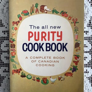 May include: A white ceramic mug with a black handle and the text "But First, Coffee" in a bold, black font. The mug is set against a blurred background, suggesting a cosy setting.