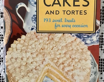 May include: A vintage cookbook titled CAKES AND TORTES 193 sweet treats for every occasion. The cover features a layered cake with white frosting on a patterned plate, surrounded by blue and white teacups and a teapot on a dark red background.