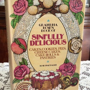 Peut inclure: Un livre de cuisine à couverture rigide intitulé Grandma Rose's Book of Sinfully Delicious Cakes, Cookies, Pies, Cheese Cakes, Cake Rolls & Pastries par Rose Naftalin. La couverture présente des illustrations de roses roses, une pêche et un gâteau.