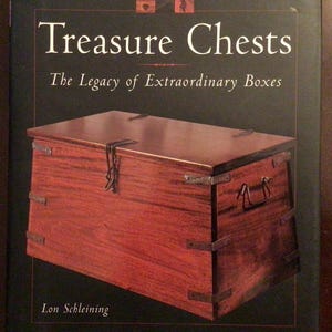 Peut inclure: Couverture de livre avec un coffre au trésor en bois et des détails métalliques. Le titre "Treasure Chests" est en blanc, avec le sous-titre "The Legacy of Extraordinary Boxes". Le nom de l'auteur, Lon Schleining, est en bas.