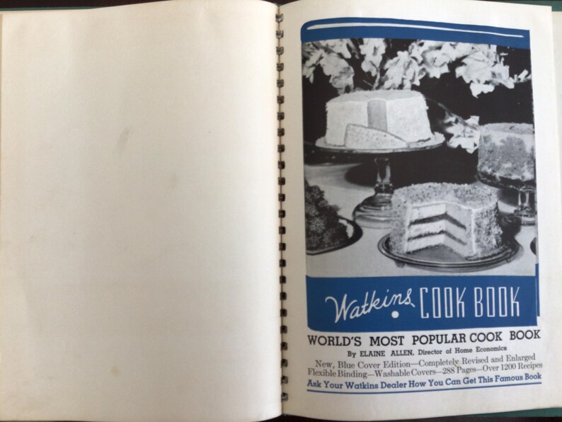 Puede incluir: Un libro de cocina Watkins de encuadernaci&oacute;n en espiral abierto con una cubierta azul y blanca que presenta fotograf&iacute;as en blanco y negro de pasteles en capas sobre pedestales. El texto dice Watkins COOK BOOK, WORLD'S MOST POPULAR COOK BOOK.