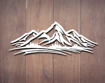 May include: White mountain range silhouette against a wood grain background. The design features multiple peaks, a line of trees, and a curved base, creating a nature-inspired wall art piece.