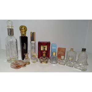 May include: Collection of perfume bottles and decorative glass containers. Includes a tall, clear bottle with a silver top, a black bottle with gold accents, and several small perfume bottles.