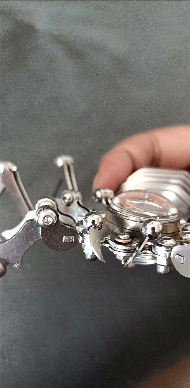 May include: A silver metal robotic spider with a clear glass dome on its back. The spider has multiple articulated legs and a detailed design.