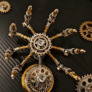 Pu&ograve; includere: Una scultura in stile steampunk composta da componenti metallici, tra cui ingranaggi, molle e bielle. Il design centrale &egrave; un ingranaggio circolare con bracci radiali, in argento e oro. Altri ingranaggi sono posizionati attorno alla struttura principale.