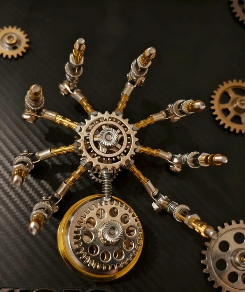 Pu&ograve; includere: Una scultura in stile steampunk composta da componenti metallici, tra cui ingranaggi, molle e bielle. Il design centrale &egrave; un ingranaggio circolare con bracci radiali, in argento e oro. Altri ingranaggi sono posizionati attorno alla struttura principale.