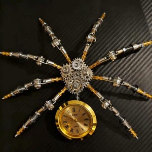Pu&ograve; includere: Una scultura in metallo in stile steampunk a forma di ragno. La scultura presenta un orologio color oro con la scritta "CAMRY" e numeri romani, circondato da braccia e ingranaggi meccanici argentati e dorati. Lo sfondo &egrave; una superficie nera strutturata.