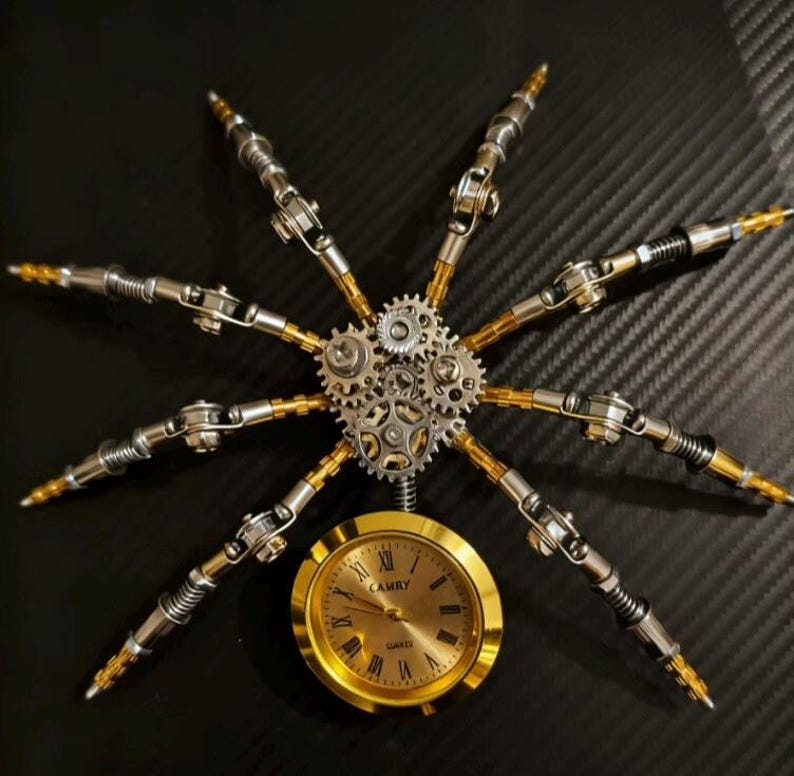 Pu&ograve; includere: Una scultura in metallo in stile steampunk a forma di ragno. La scultura presenta un orologio color oro con la scritta "CAMRY" e numeri romani, circondato da braccia e ingranaggi meccanici argentati e dorati. Lo sfondo &egrave; una superficie nera strutturata.