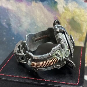 May include: A silver and copper steampunk-style watch with a detailed, intricate design. The watch has a large, round face and a thick, textured band.