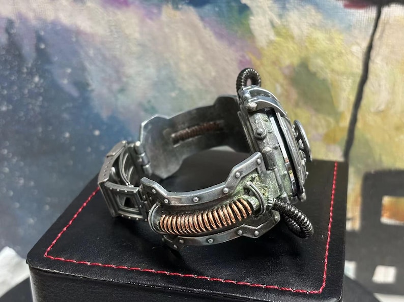 May include: A silver and copper steampunk-style watch with a detailed, intricate design. The watch has a large, round face and a thick, textured band.