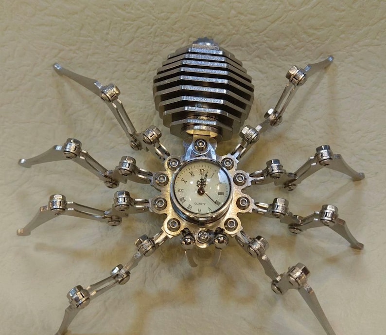 May include: A silver metal spider clock with a round clock face and black Roman numeral hour markers. The clock face says "Quartz".