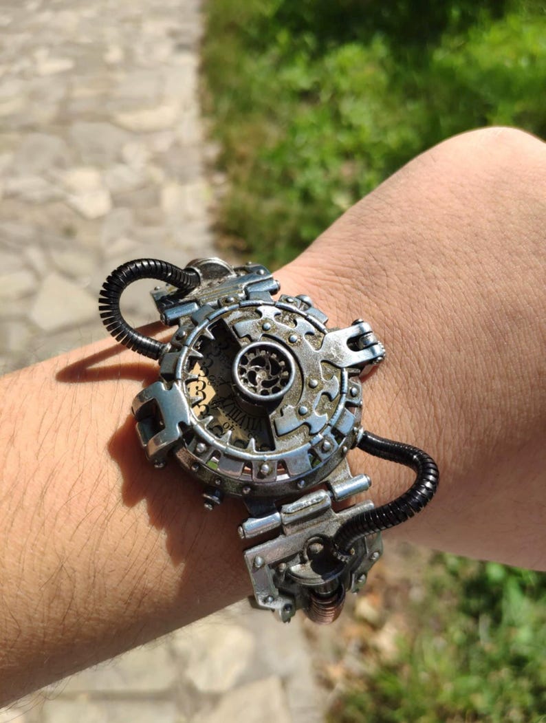 Op de afbeelding: Een zilveren steampunk-armband met een cirkelvormig tandwielontwerp en zwarte slangaccenten.