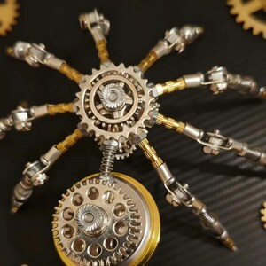 Pu&ograve; includere: Una scultura in metallo in stile steampunk raffigurante un ragno meccanico. La scultura presenta ingranaggi, molle e zampe articolate con toni argento e oro. Il ragno &egrave; ambientato su uno sfondo scuro con ingranaggi aggiuntivi.