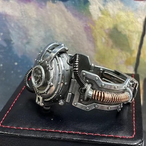 May include: A silver steampunk-style wristwatch with a round face and intricate gears. The watch has a copper-colored band with a textured surface.
